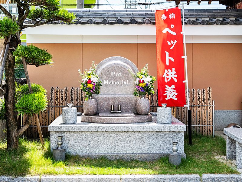 芝生に囲まれた實成寺のペット供養塔と後ろに卒塔婆